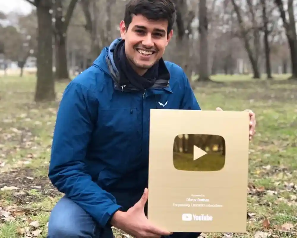 Dhruv Rathee smiling and holding his YouTube Gold Play Button award in a park.