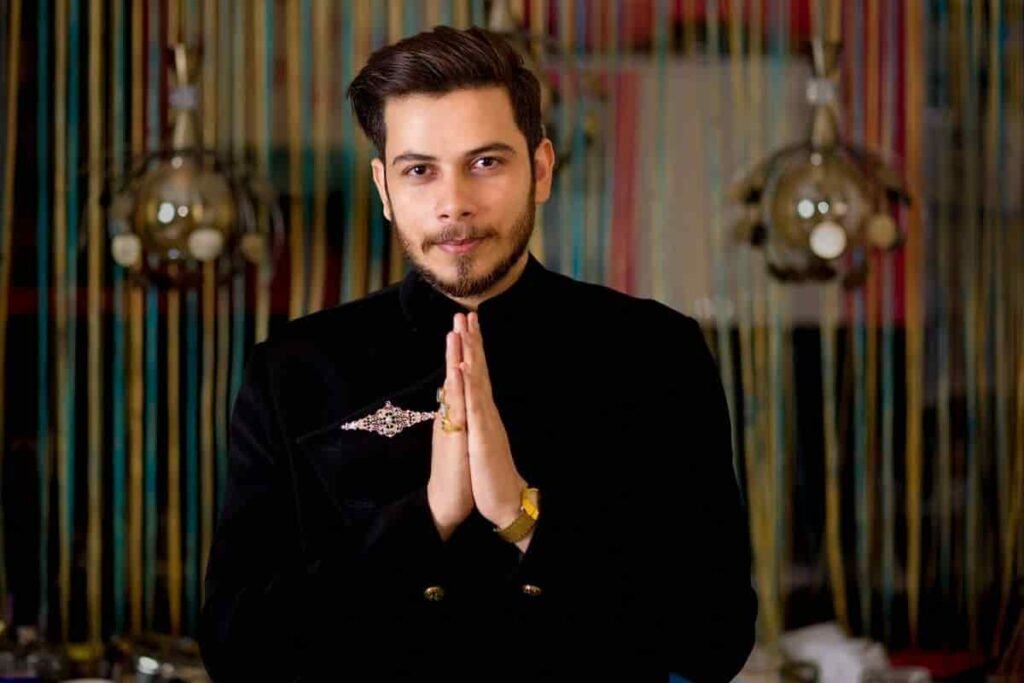 Nitish Rajput standing in a black outfit with hands folded in a formal pose.