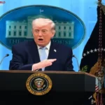 Donald Trump stands at a White House podium during a press briefing, with the presidential seal and flags visible behind him.