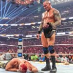 WWE wrestler standing over an opponent in the ring during a championship match.