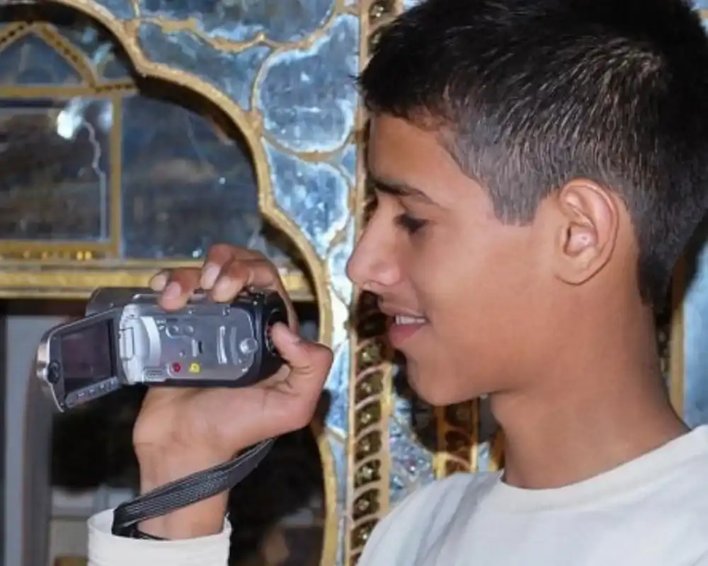 Young Dhruv Rathee holding a camcorder in front of ornate mosque architecture.