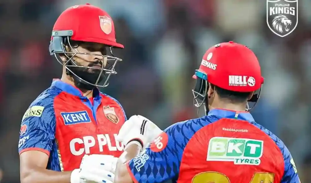Two Punjab Kings batters in red helmets and match kits during an on-field discussion in the IPL.
